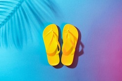 Minimalist flat lay photo of pair of beach flip-flops with copy space. Yellow flip-flops on the blue background with palm tree shadow.