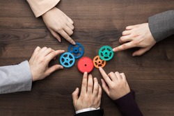 Teamwork concept. Different hands of men and women connect colorful gears into working mechanism on the brown wooden table background. Each has its own role in problem-solving. Experience exchange