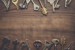 many different keys on brown wooden background with copy space in the centre