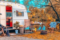 trailer of mobile home or recreational vehicle stands on shore of pond in camping in autumn near table set, concept of family local travel in native country on caravan or camper van and camping life