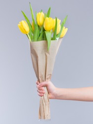 Children hand holding flowers over gray background. Bouquet of yellow tulips for Birthday, Happy mothers or Valentines day.