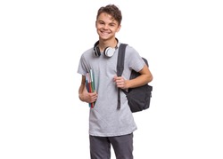 Happy teen boy with headphones and backpack holding books, isolated on white background. Smiling child looking at camera. Emotional portrait of handsome teenager guy Back to school.