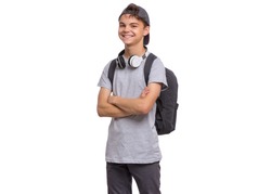 Happy teen boy in cap with headphones and backpack, isolated on white background. Smiling child with folded arms looking at camera. Emotional portrait of handsome teenager guy Back to school.