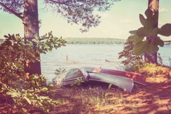 Canoes pulled up on the shore, with kids playing in the lake. Vintage Instagram effect.