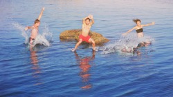 Happy crazy guys and girl jumping in natural sea pool from rock at sunset. Young fearless group of three friends fun diving in ocean water from cliff. Summer lifestyle and adventure vacation concept