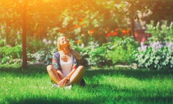 Happy free young woman sitting outdoors in yoga position with closed eyes on summer park grass Calm girl enjoy smile and relax in spring city air. Mindset inner light peace concept. 