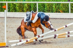 Young rider falling from horse during a competition. Horse show jumping accident. Equestrian sport background. 
