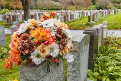 Flowers on a headstones in a cemetery with hundreds of tombstones in the background