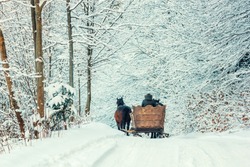 Winter landscape - view of the snowy road with with a horse sleigh in the winter mountain forest after snowfall