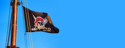 The pirate flag or the Jolly Roger - old shabby black flag with a skull waving on the mast of a sailing ship