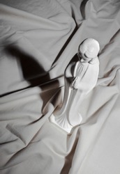 White ceramic statue of the Virgin Mary on white cloth with shadow