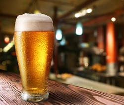 Glass of light beer on a dark pub.