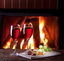 Romantic still life near the fireplace. Glasses of wine, cheese and nuts.