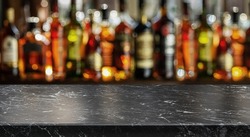 Grey table top and beautiful bokeh shelves with alcohol bottles at the background. Bar concept.