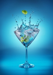 Martini glass with amazing splash as the result of olive berries falling down in it. Blue background.