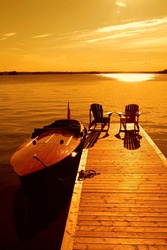 Two empty lounge chairs on dock with anchored vintage motor boat