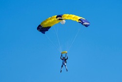 Parachutist with  yellow and blue parachute against a blue sky