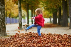 Adorable preschooler girl walking and kicking fallen leaves in Tuileries garden in Paris, on a fall day. Happy child enjoying autumn day. Fall season in France. Outdoor autumn activities for kids