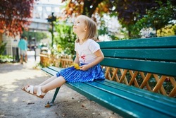 Happy cheerful toddler girl sitting on the bench on a street of Paris, France