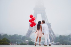 Beautiful romantic couple in love with bunch of red balloons together near the Eiffel tower in Paris on a cloudy and foggy rainy day