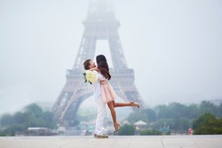 Beautiful romantic couple in love with bunch of white roses having fun near the Eiffel tower on a cloudy and foggy rainy day. Paris, France
