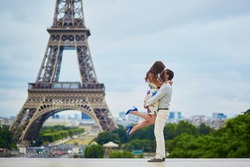 Loving couple having a date near the Eiffel tower. Romantic jump hug. Tourists on vacation or during their honeymoon in Paris, France