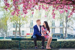 Romantic couple having a date in Paris on a spring day with beautiful cherry blossoms in the background. Tourists enjoying their vacation in France. Romantic date or traveling couple concept