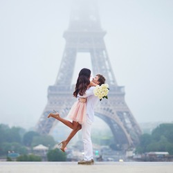 Happy couple with white roses near the Eiffel tower in Paris. Tourists enjoying their vacation in France. Romantic date or traveling couple concept