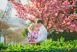 Beautiful romantic couple under blooming cherry tree on a spring day with Eiffel tower in background in Paris, France