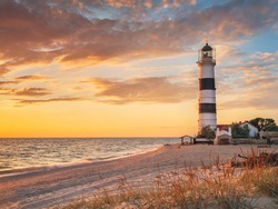 golden paints of sunset in scene of summer beach and lighthouse with illuminated grass