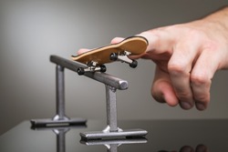 A man plays with a fingerboard on a gray metal railing.