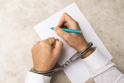 A man in handcuffs writes a will or confession of a crime, the concept of obtaining consent under the influence of pressure on people