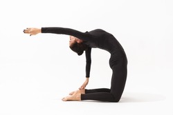 A woman in a black tracksuit practicing yoga performs a variation of the Ushtrasana exercise, camel pose with outstretched arm, on a white background