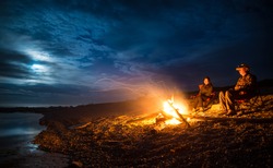 Campfire on a rocky beach with a couple sitting