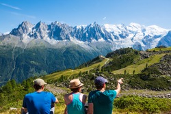 French  Alps summer travel. Three friends (unidentified people, back view) admiring beautiful snow covered Mont Blanc mountains range.  France nature hiking tourism background. Active vacation concept