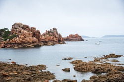 Beautiful panoramic view of Pink Granite Coast between Perros-Guirec and Ploumanach. Cliffs, boats and lighthouse on horizon. Cotes-d'Armor, Brittany, France