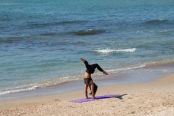 Silhouette of unrecognizable young woman practicing handstand at sea beach. Tel-Aviv, Israel. Fitness in nature background. Healthy lifestyle concept.