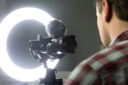 A man streaming through the Internet, video recording with a mirrorless camera and ring light.