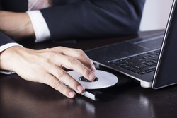 Business's hand holding Disk insert to laptop computer 