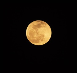 Reddish full moon at low altitude in the sky. Reddish since light other then red is easily scattered by particles in the atmosphere, and red light becomes the most prominent source of color.