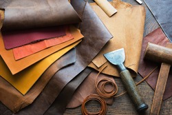 Leather craft or leather working. Selected pieces of beautifully colored or tanned leather on leather craftman's work desk . Piece of hide and working tools on a work table.