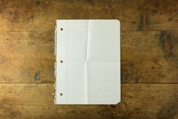 Folded piece of white note pad paper, opened on old wooden desk. Isolated.