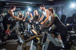 Group of attractive women and men pedaling on a stationary bikes at the gym.