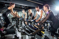 Group of sporty women and men training on exercise bikes together at gym.