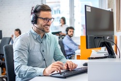 Young male technical support dispatcher in call center. Man in call center with headset helping customer.