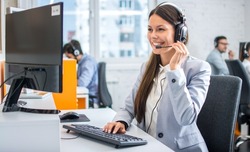 Friendly female helpline operator in call center. Young woman working in call center and holding microphone on headset with hand.