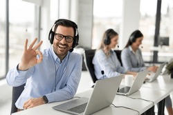Portrait of handsome bearded business man with headset showing OK sing at call center office