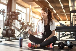 Young sporty woman listening to music on smartphone in gym. Break after hard workout.