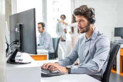 Young handsome male customer support phone operator with headset working in call center.