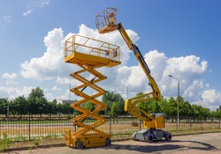 Yellow self propelled articulated boom lift and scissor lift on background of street with trees and sky